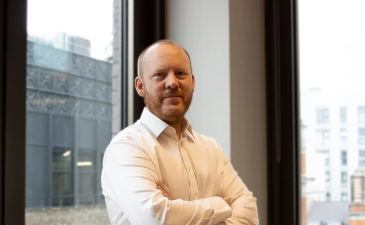 Dan McNally by a window with his arms crossed.
