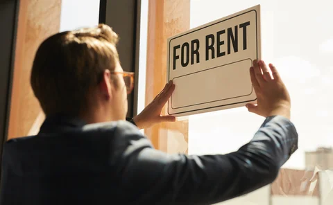 Back view at real estate agent hanging FOR RENT sign on window of house or apartment