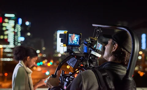 Behind the scenes shot of a camera operator shooting a scene with a woman at night