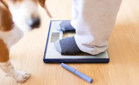 Woman checking her weight on a scale at home, with a semaglutide injection pen nearby, indicating her commitment to managing obesity and achieving weight loss goals