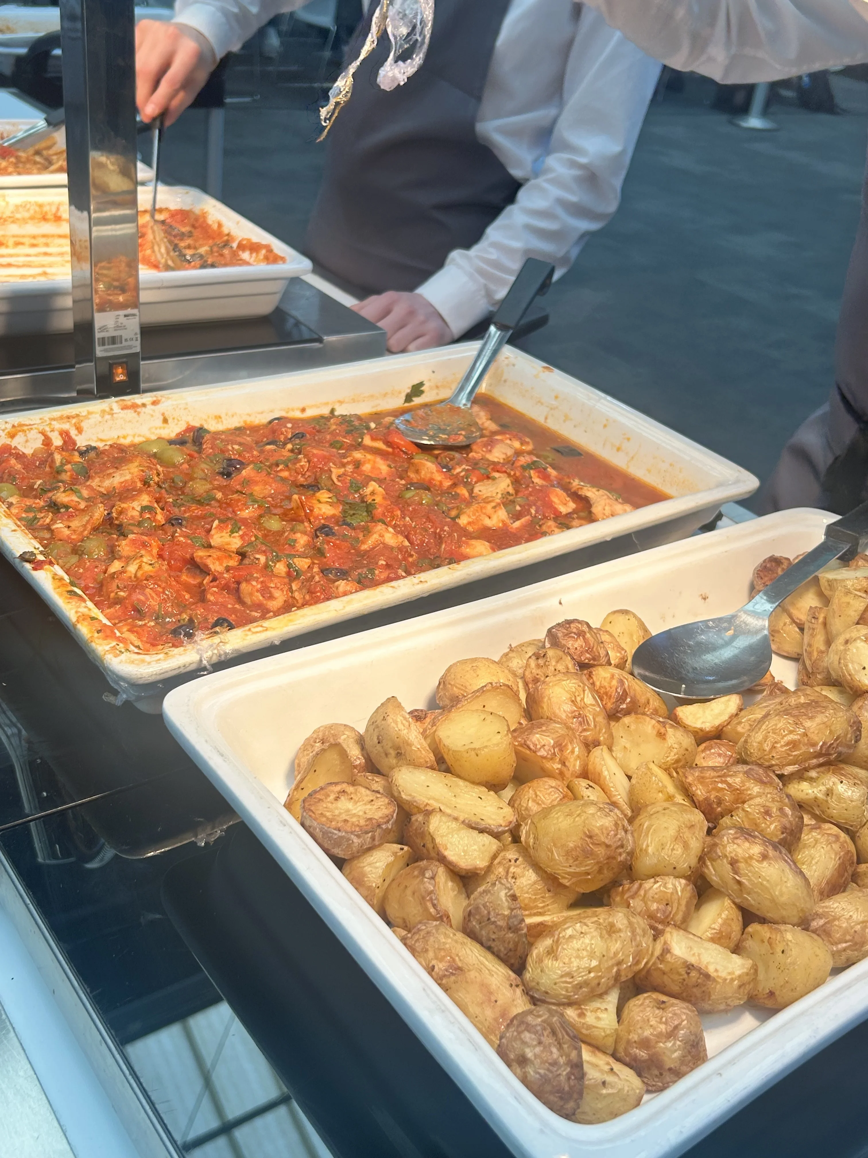 Two servish dishes with chicken cacciatore on the left and roast potatoes on the right.